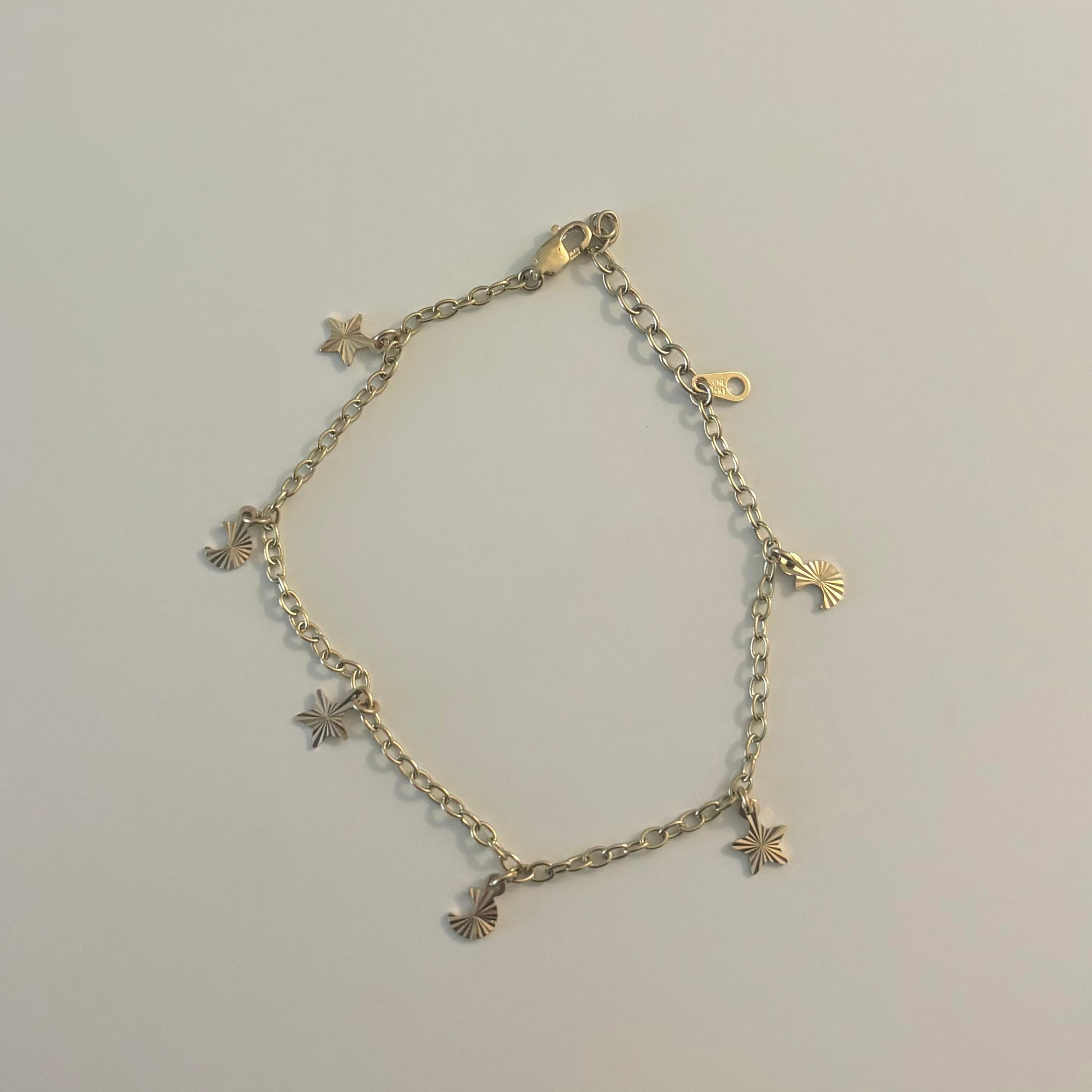 Gold bracelet with star and cross designs on a light gray surface.