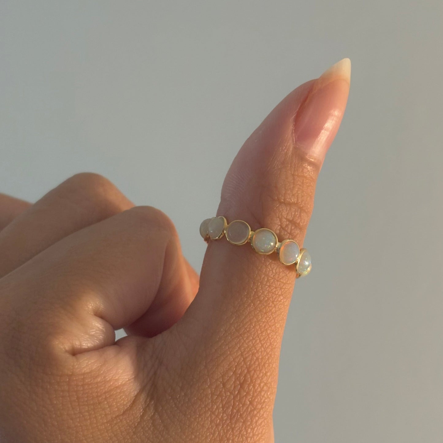 Close-up of a hand wearing a delicate ring with small stones on a neutral background