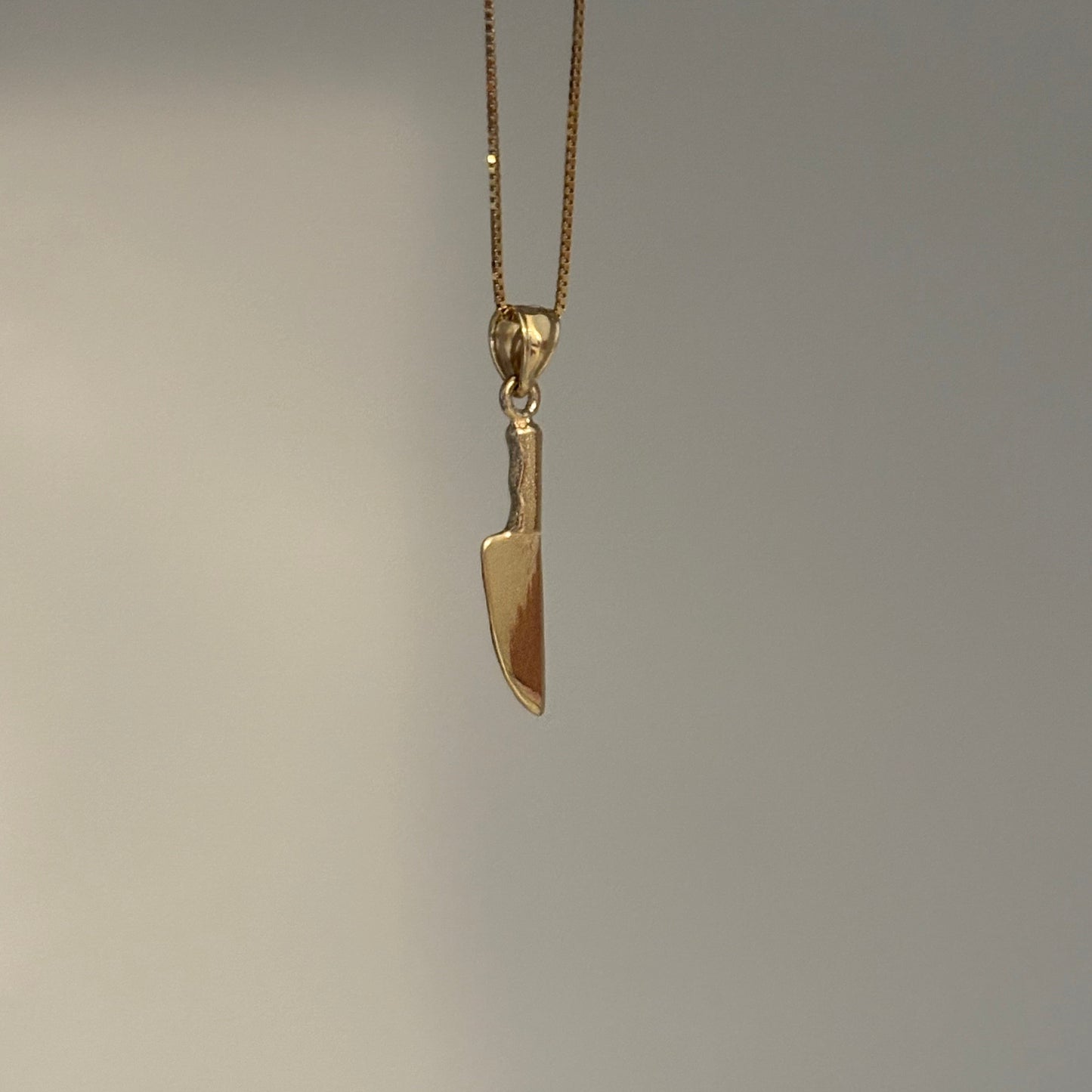 Gold knife-shaped pendant on a chain against a gray background