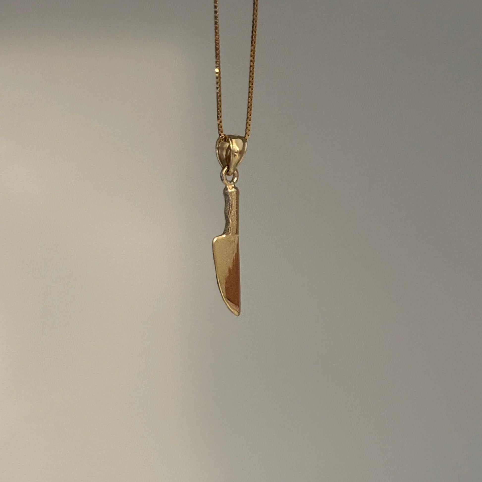 Gold knife-shaped pendant on a chain against a gray background