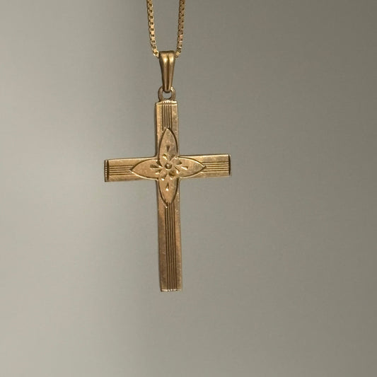 Gold cross pendant on a chain against a gray background