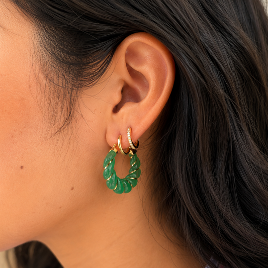 Close-up of a person wearing green jade hoop earrings with a blurred background