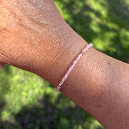 Person wearing a pink beaded bracelet with a blurred green outdoor background