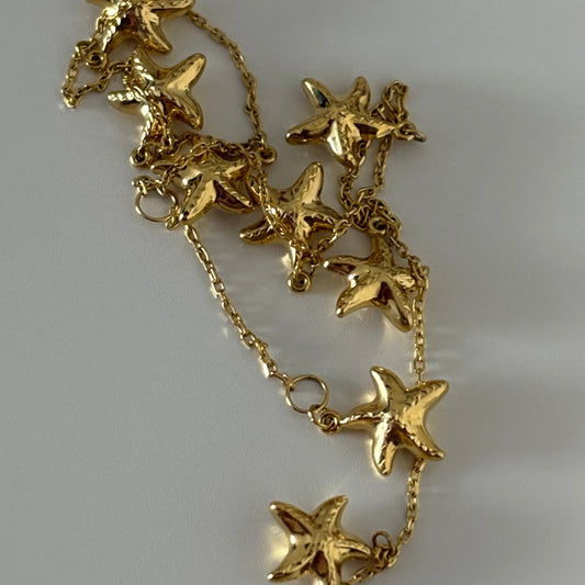 Gold necklace with starfish pendants on a light gray background