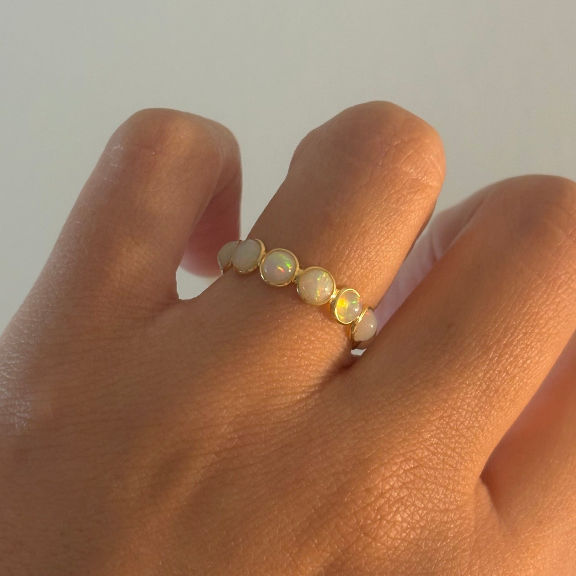 Hand wearing a ring with pearls on a plain background