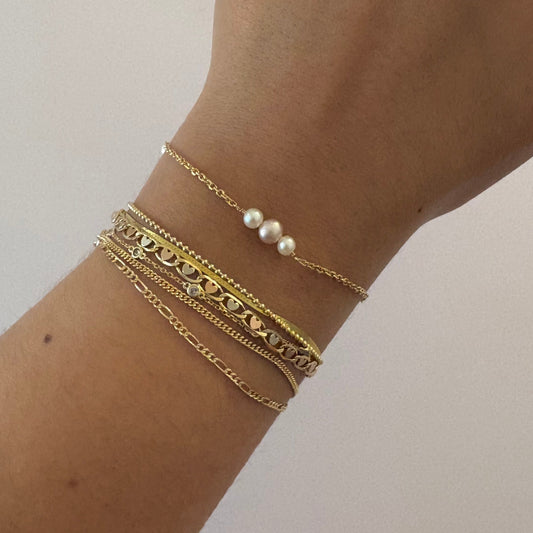 Hand wearing multiple gold bracelets on a plain background
