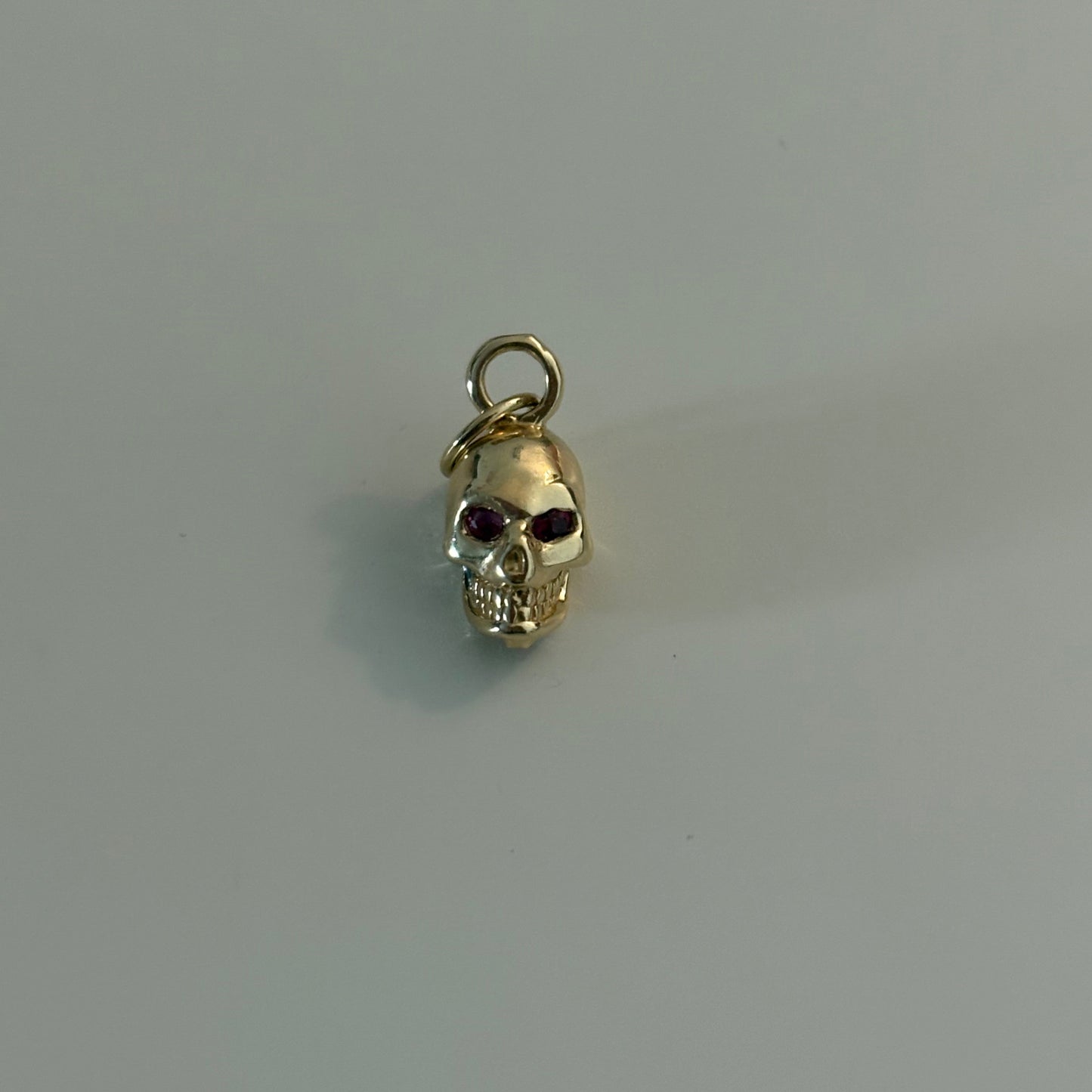 Gold skull charm with red gemstone on a gray background