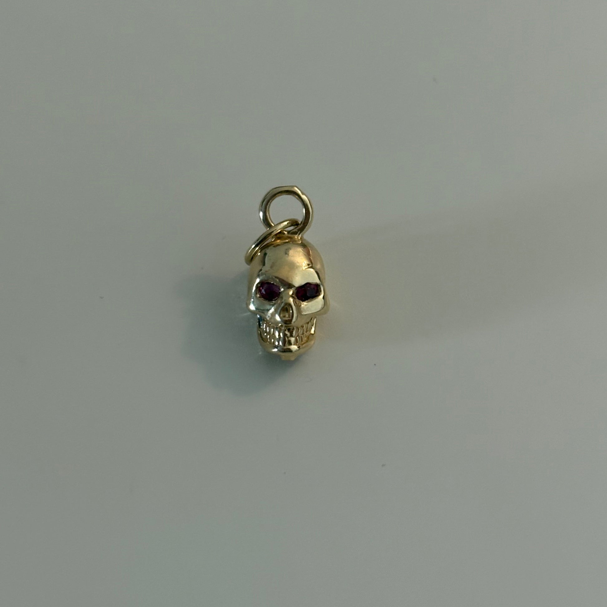 Gold skull charm with red gemstone on a gray background