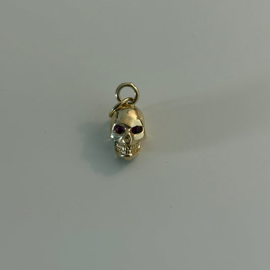 Gold skull charm with red gemstone on a gray background