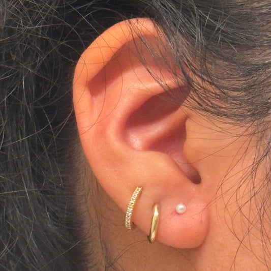 Close-up of an ear with gold hoop earrings and a pearl stud.