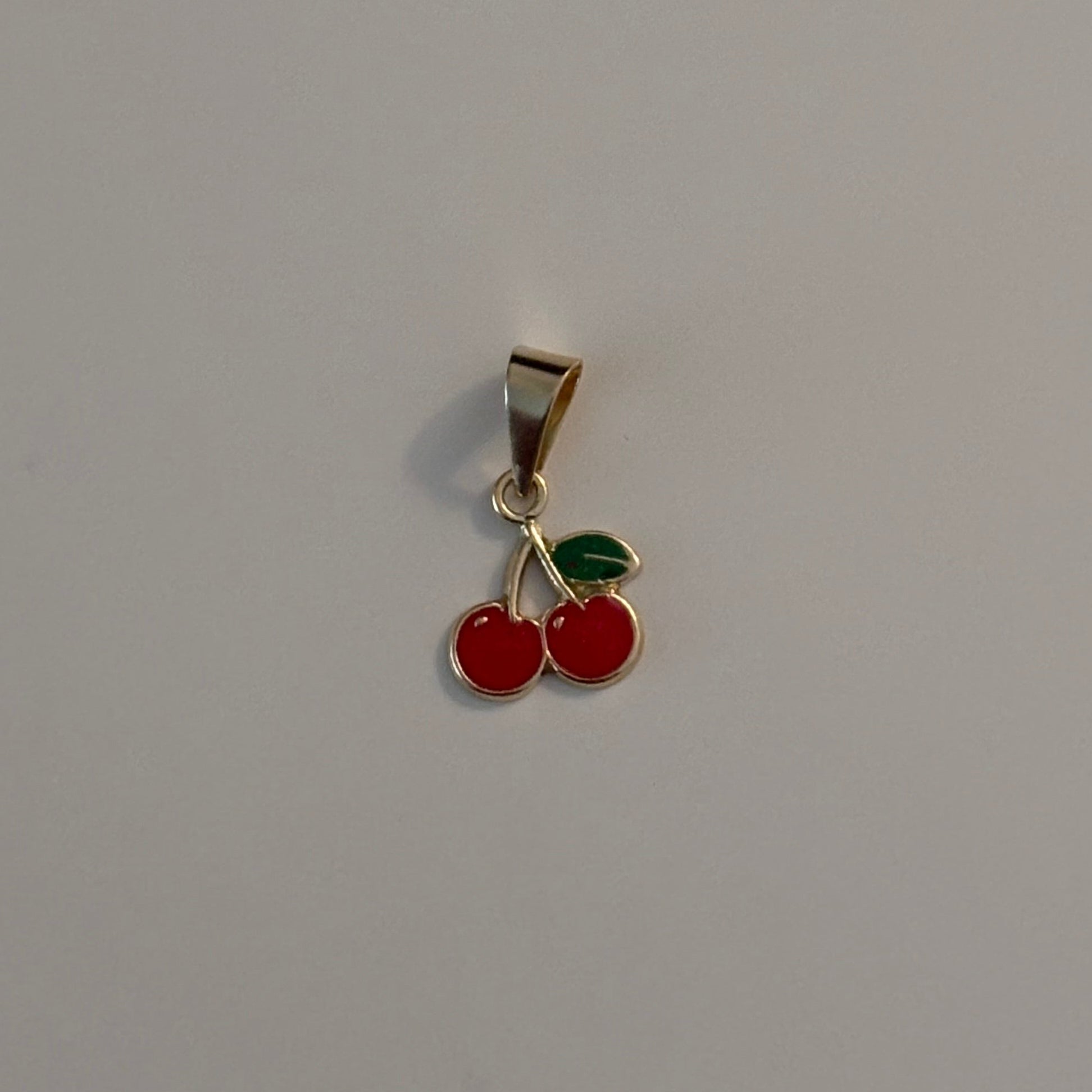 Gold pendant with two red cherries on a gray background
