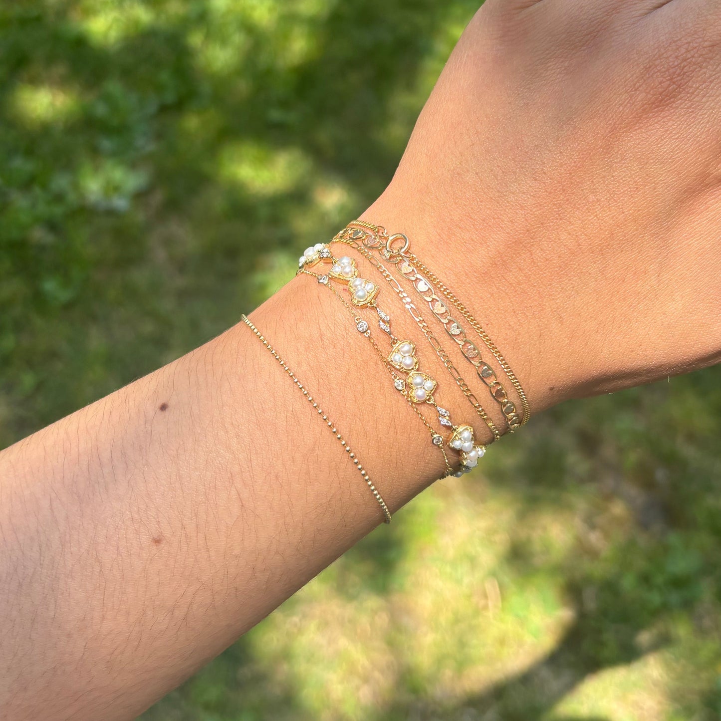 Hand wearing multiple bracelets with a blurred green background