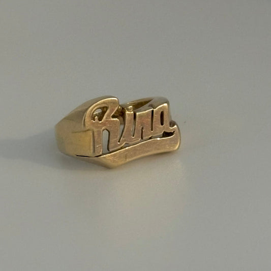 Gold ring with 'rina' engraving on a gray background