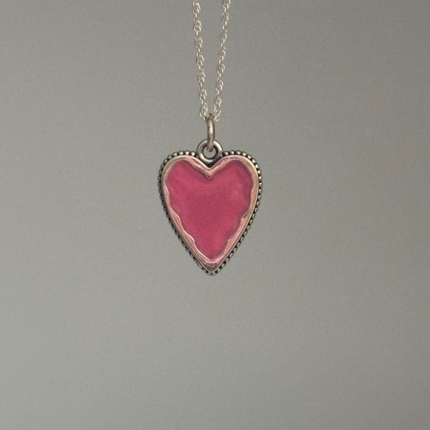 Heart-shaped pink pendant on a chain against a gray background