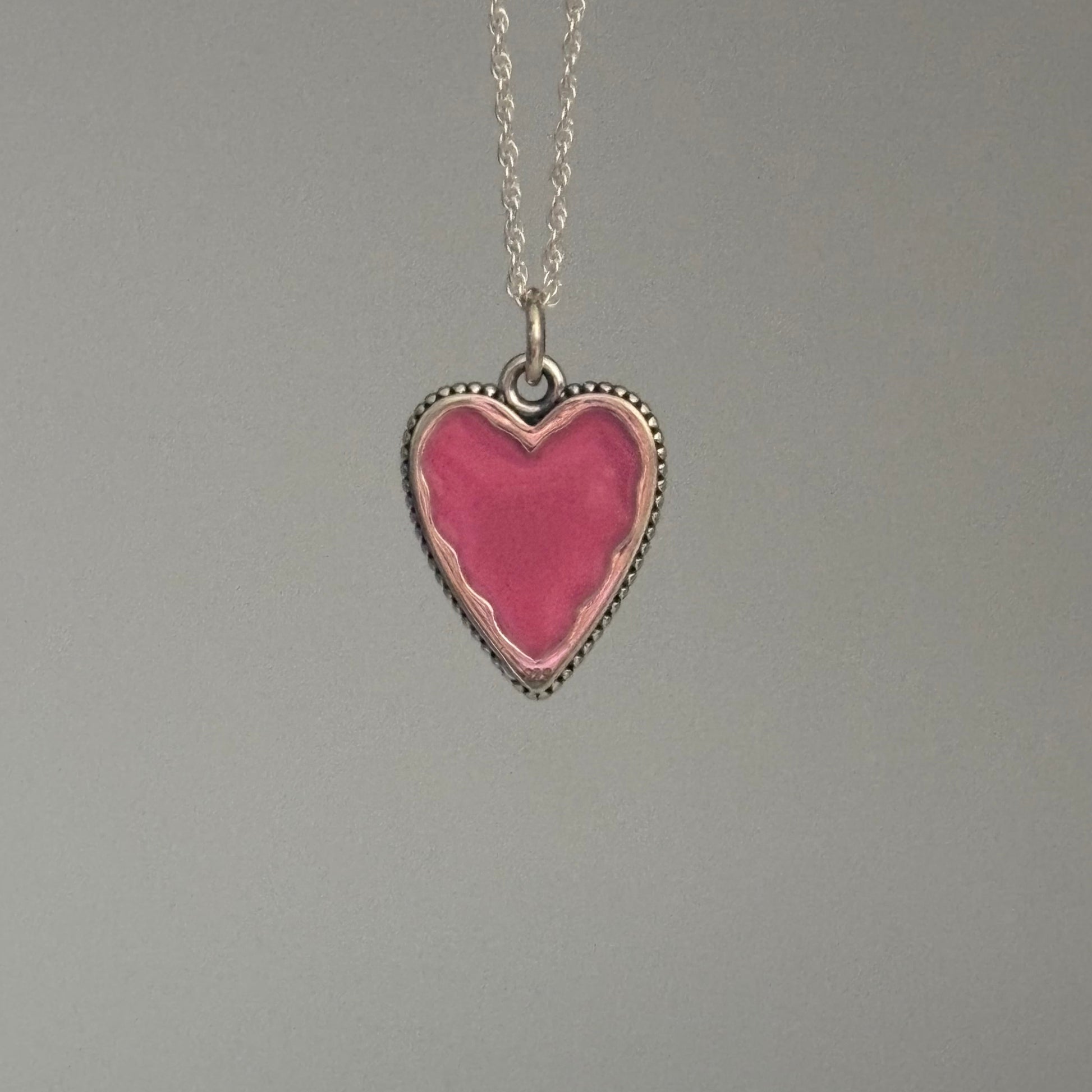 Heart-shaped pink pendant on a chain against a gray background