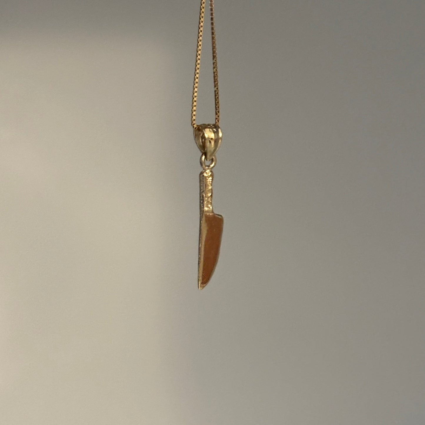 Gold knife-shaped pendant on a chain against a gray background