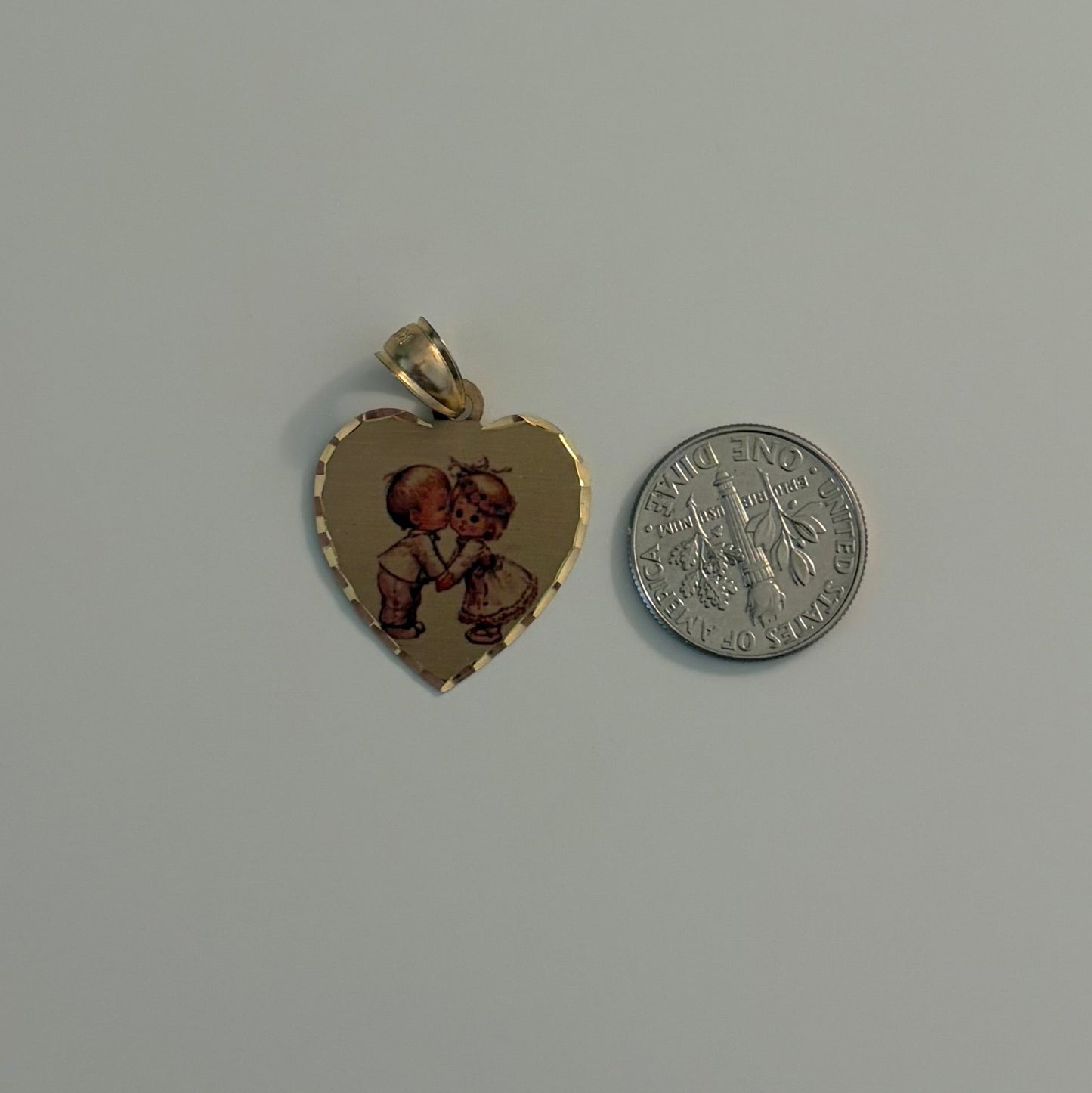 Two heart-shaped gold pendants with red stones on a gray surface, one next to a silver coin for size comparison.