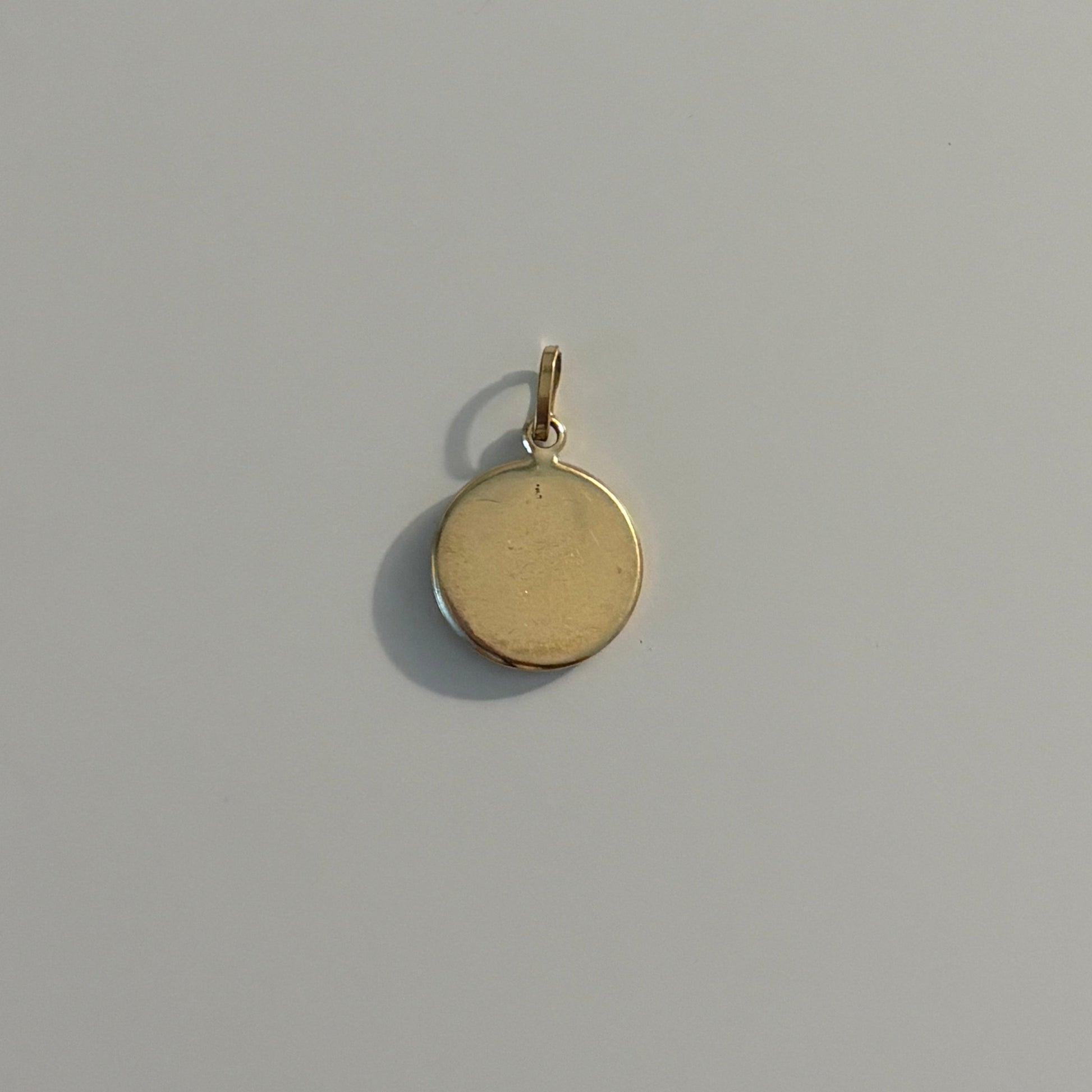 A small round gold pendant charm with a flat, polished surface and a top loop, shown on a plain light gray background.