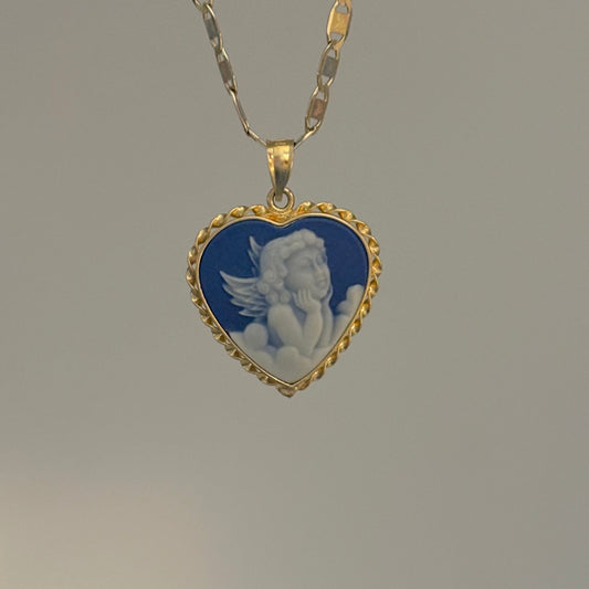 Heart-shaped pendant with angel design on a gold chain against a gray background
