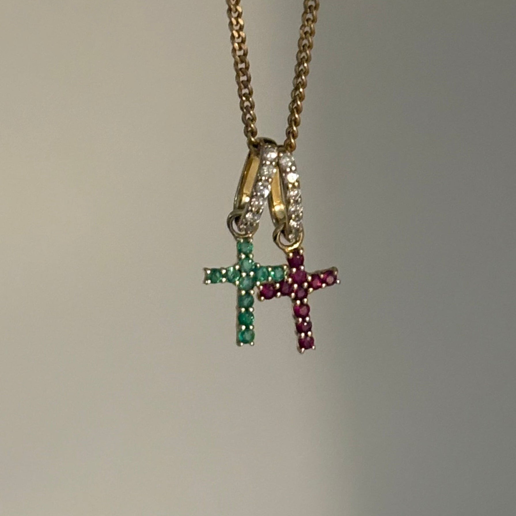A gold chain necklace with a multi-pendant set featuring three small cross charms, each colored green, pink, and gold with clear rhinestones, shown against a plain light gray background.
