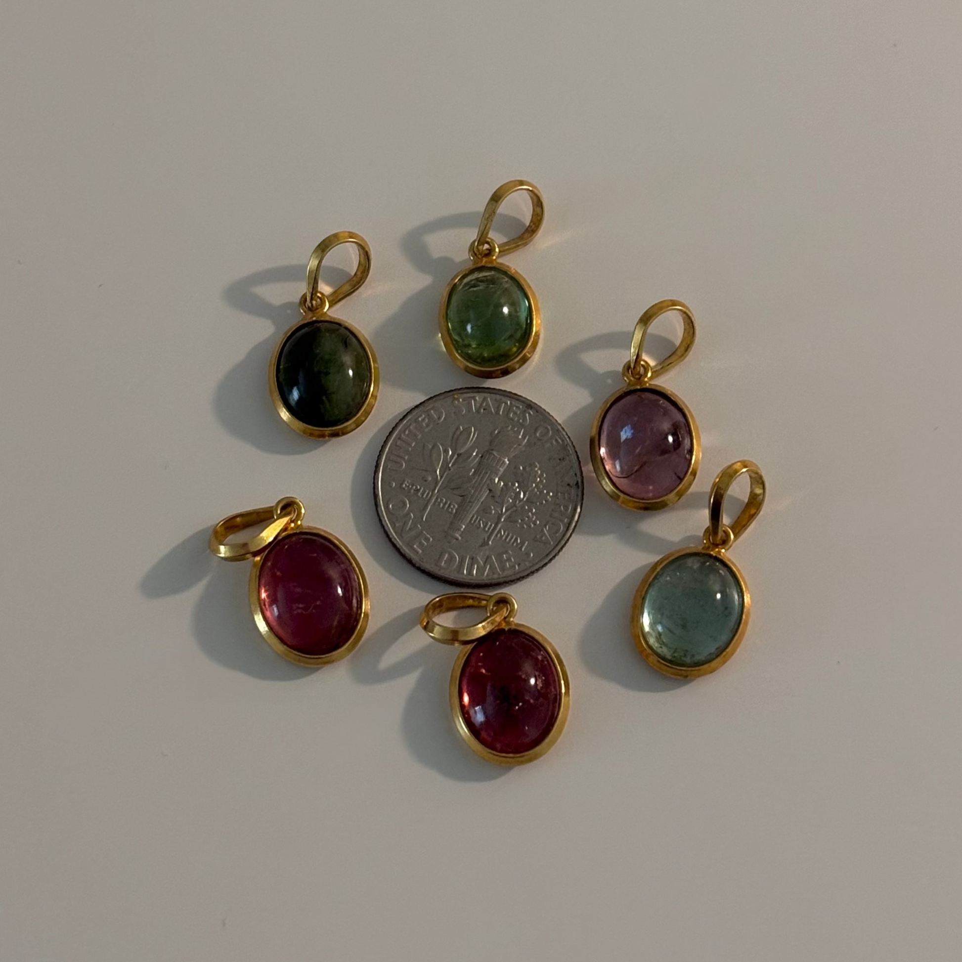 Six small oval gemstone pendants in gold-tone settings arranged around a silver coin on a plain light background.