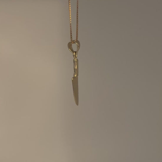 Gold knife-shaped pendant on a chain against a gray background