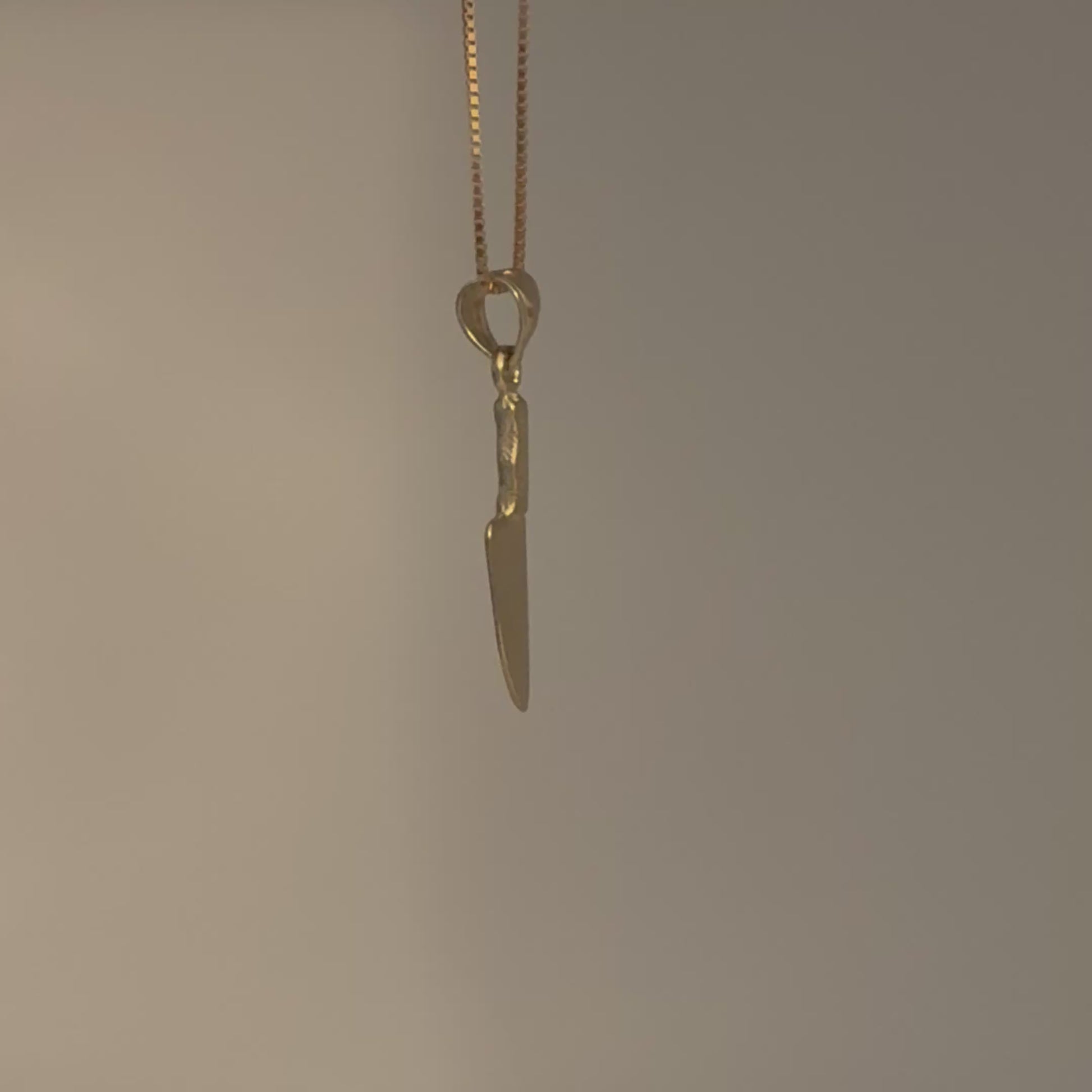 Gold knife-shaped pendant on a chain against a gray background